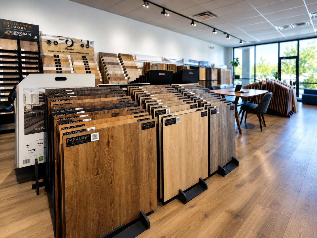 Flooring showroom racks holding upright wood-look plank samples, with a consultation table by the front windows.