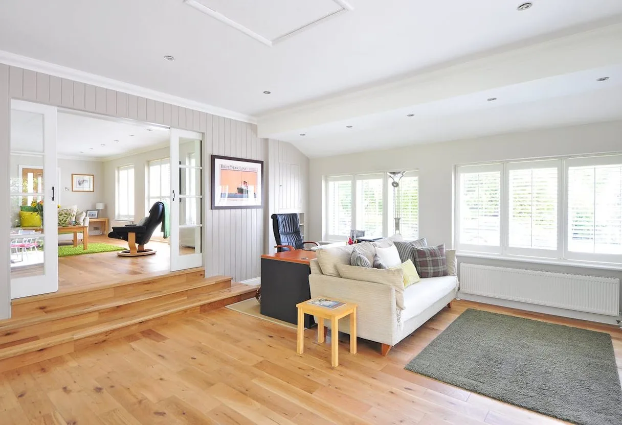 Bright open-plan living room with wide-plank light oak hardwood floors, a cream sofa and a grey area rug.